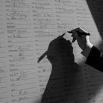 Ein Schwarz-Weiß-Foto zeigt eine Hand, die gerade ihre Unterschrift auf eine große Liste von anderen Unterschriften setzt.