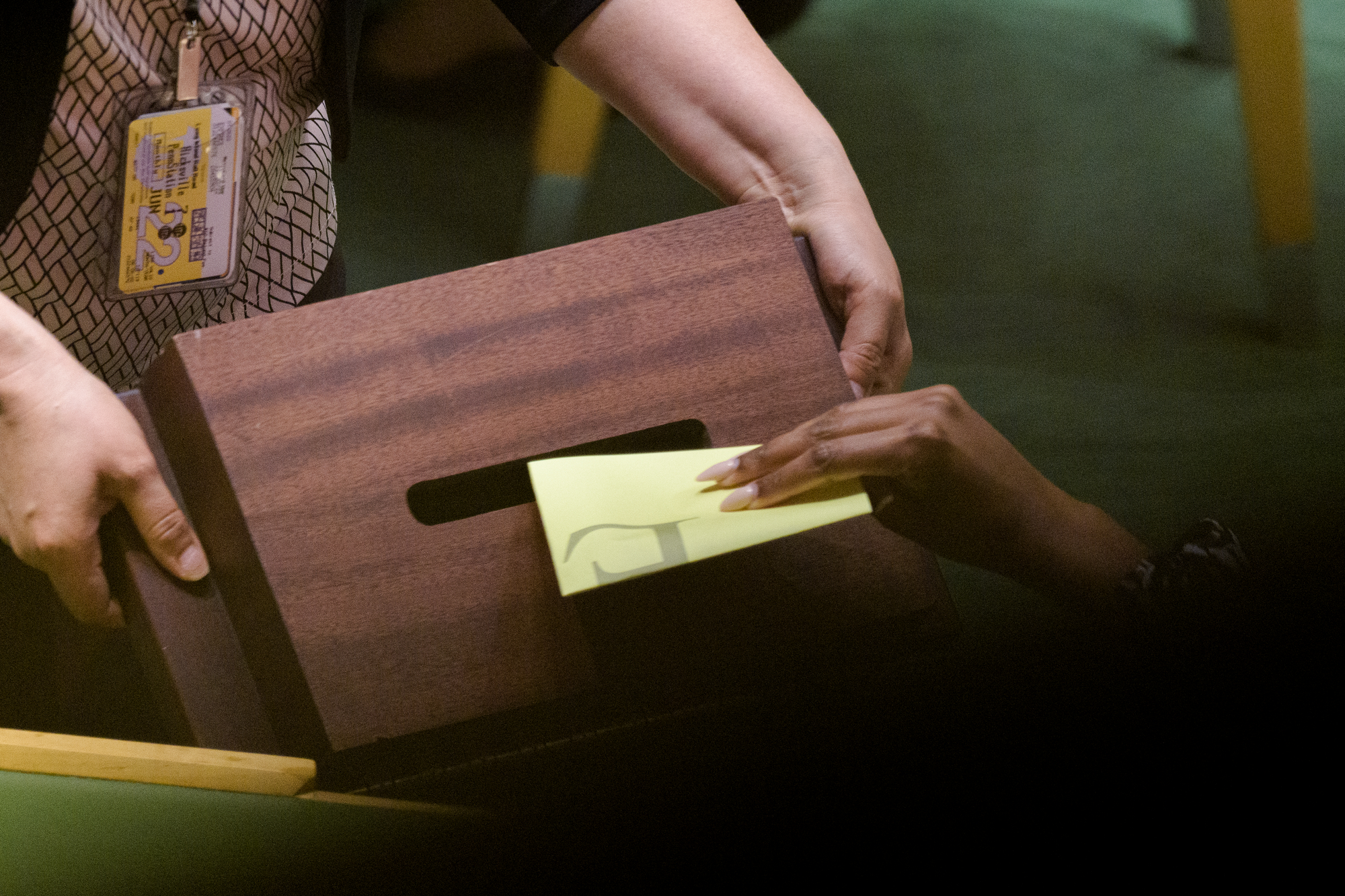 Eine Hand steckt einen gefalteten Zettel in eine Wahlurne.