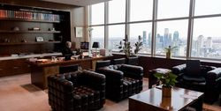 Blick ins Büro mit Ledersesseln, Bücherregal und Fensterfront mit Sicht auf die Skyline von Queens.