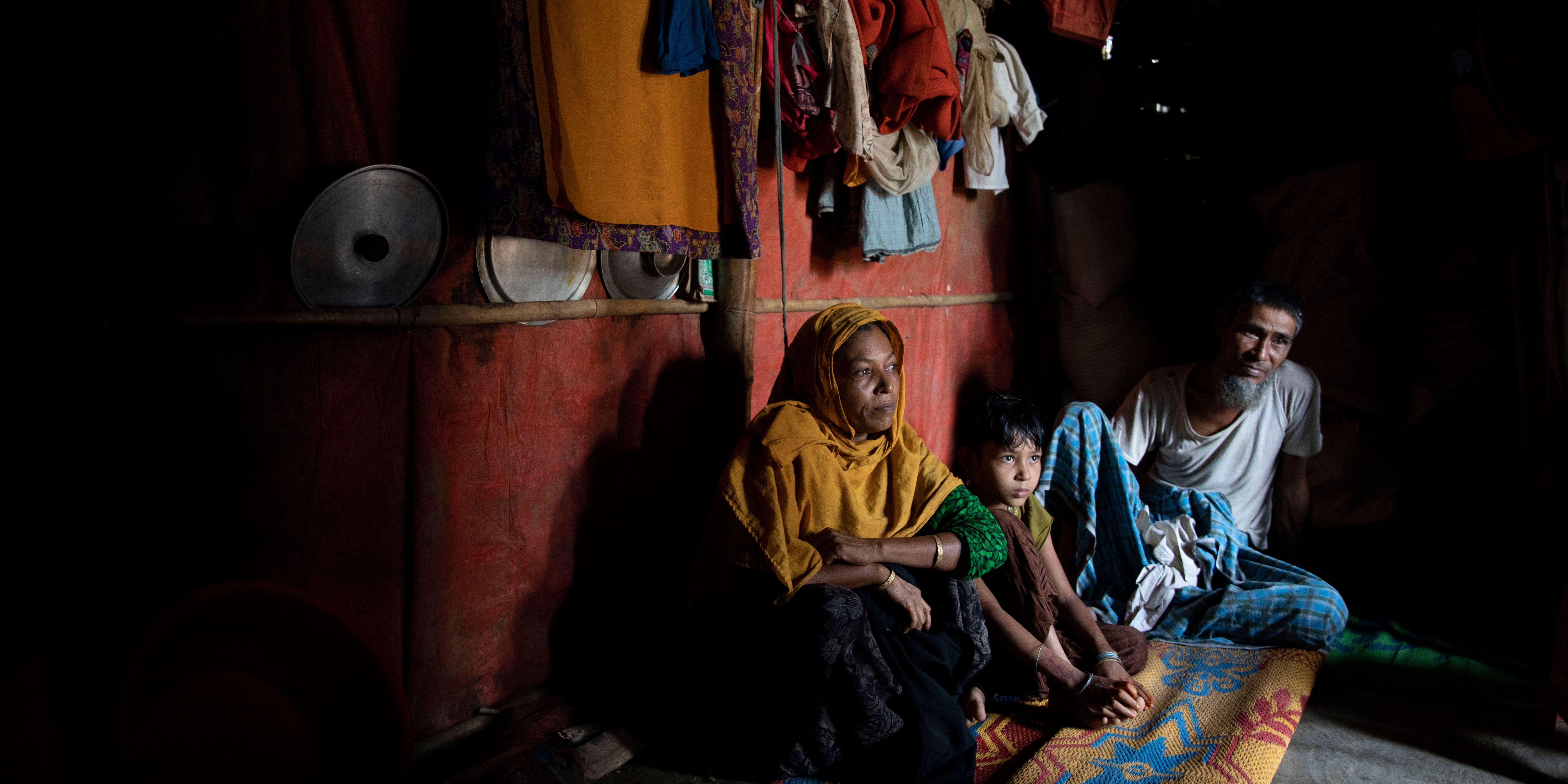 Eine Familie der Rohingya sitzt in einer dunklen Hütte auf dem Boden vor ihren wenigen Habseligkeiten.