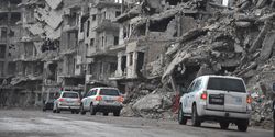 Drei UN-Fahrzeuge fahren durch einen von Bomben zerstörten Stadtteil von Homs.
